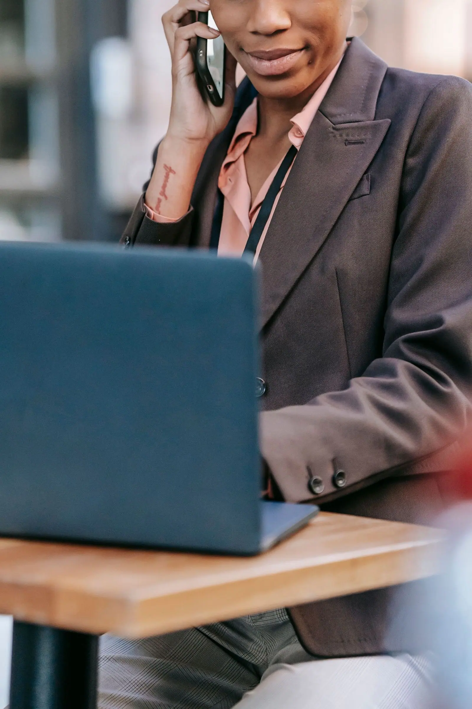 A person holds a phone to their ear while working at a laptop on a wooden table.
