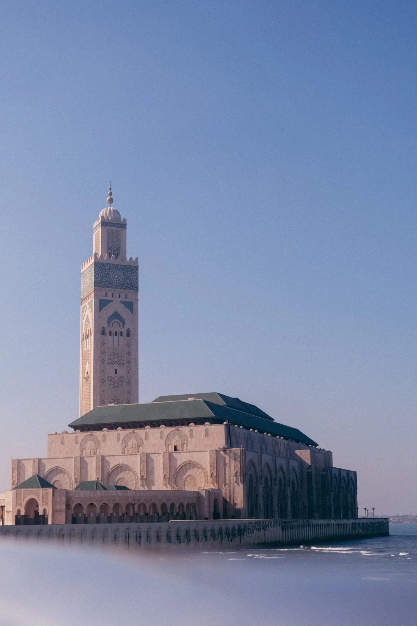 The Hassan II Mosque stands on the Atlantic edge of Casablanca, its minaret rising above a green roof.