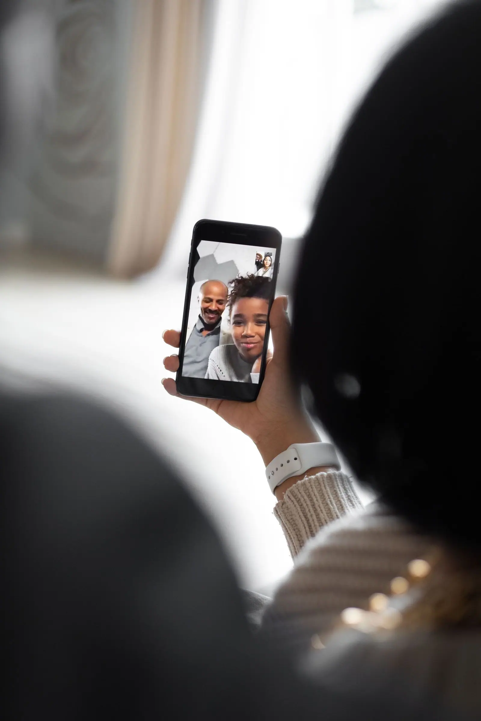 Over a person’s shoulder, a phone screen shows a man and a child during a video call.